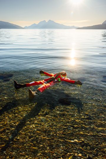 person floating in a fjord under the midnight sun with mountains in the background