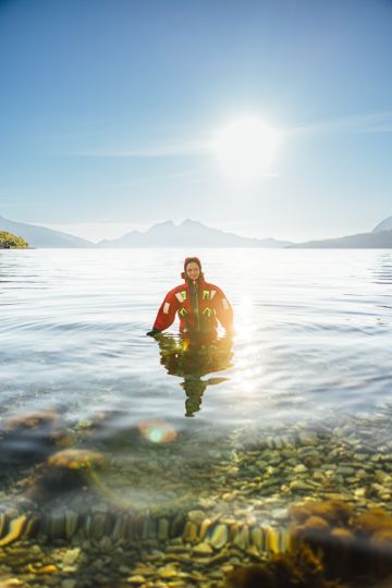 person walking up from the sea in a fjord under the midnight sun with mountains in the background