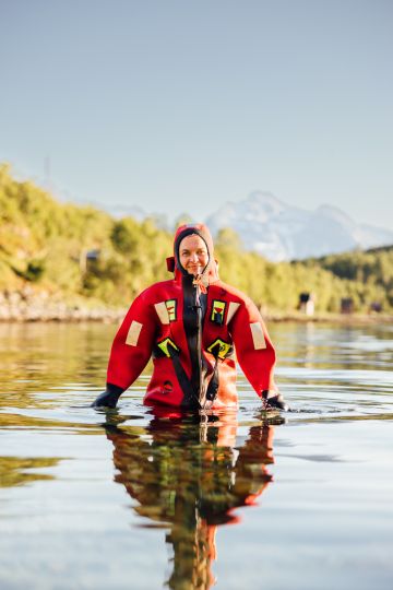 person walking up from the sea in a fjord under the midnight sun with mountains in the background