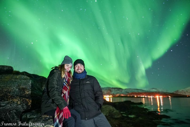 Two people standing under Northern lights