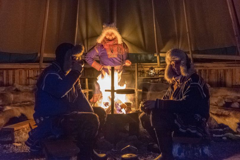 people sitting around camp fire inside of Lavvo