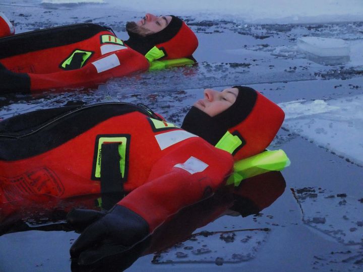 People floating over frozen lake in theraml warm suits