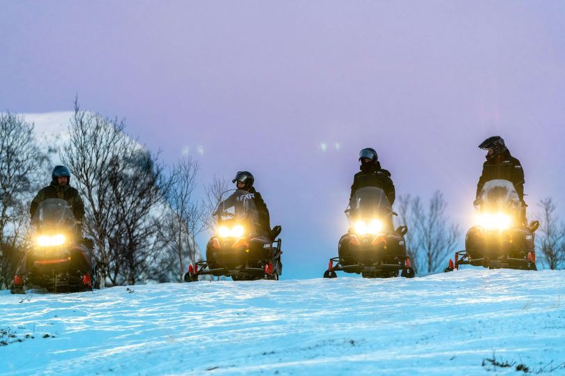 People driving snowmobiles through snowy nature.