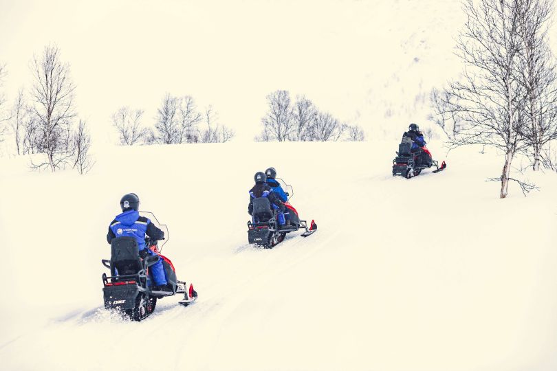 People driving snowmobiles through snowy nature.