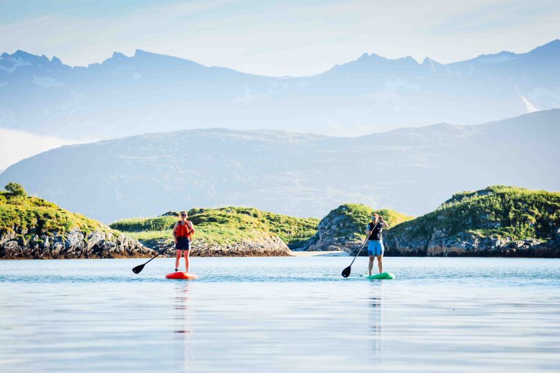 two people paddleboarding along small islands with mountains in the background