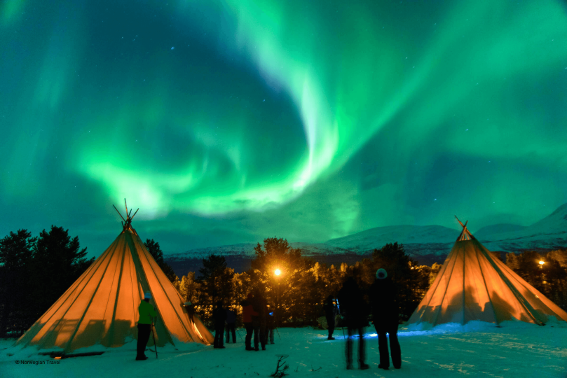 People watching Northern lights next to two Lavvos