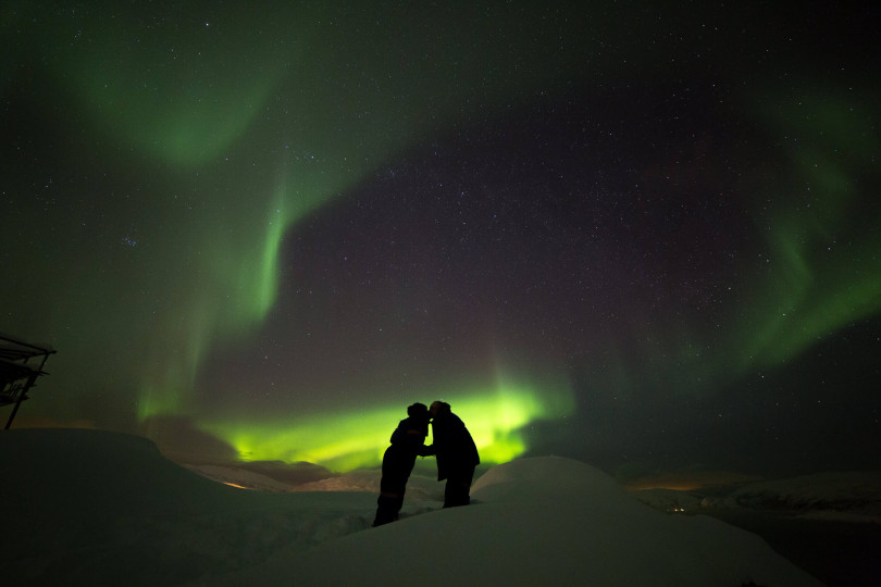 Two people standing under Northern lights
