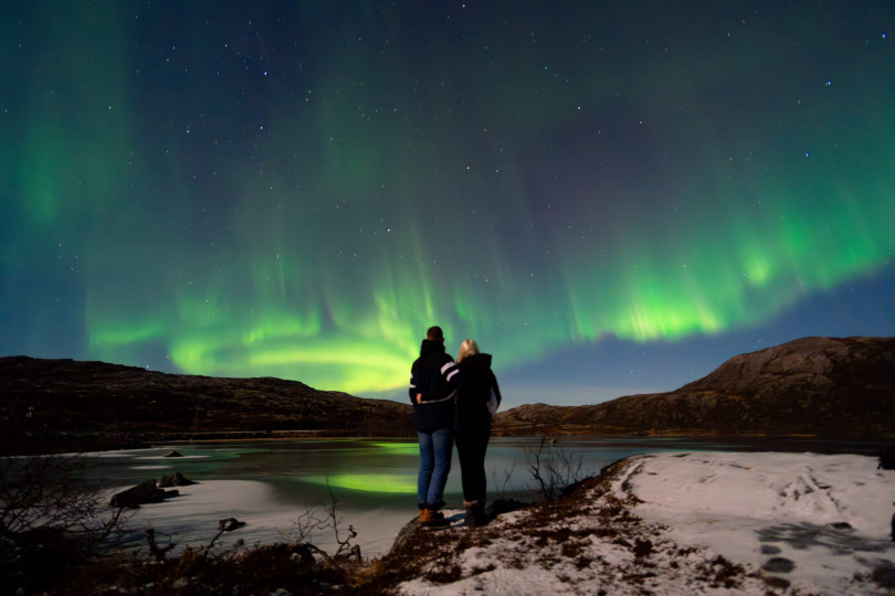 Two people standing and watchig at Northern lights