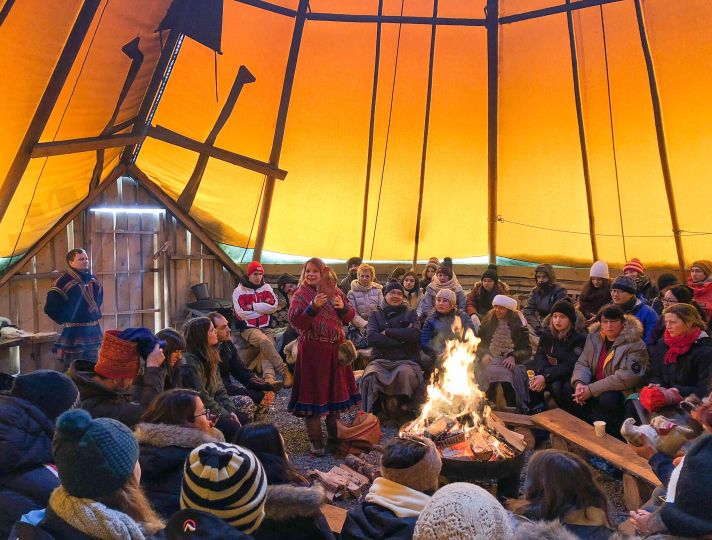 People sitting around fire inside of Lavvo