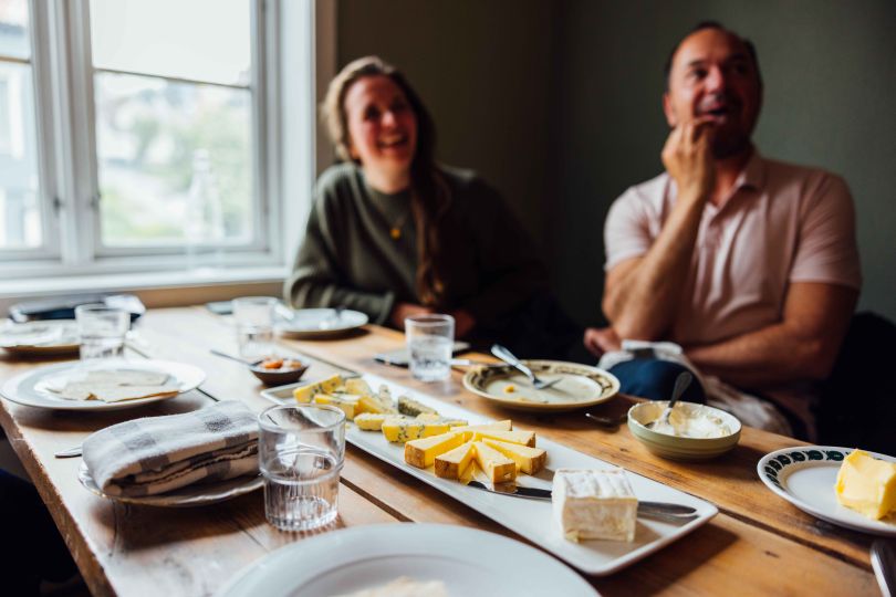 two people sitting by a table eating different types of Norwegian cheese