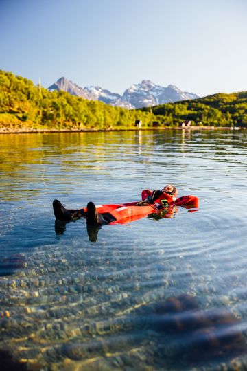 person floating in a fjord under the midnight sun with mountains in the background