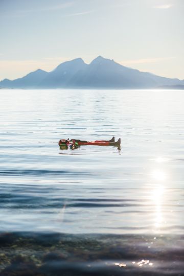 person floating in a fjord under the midnight sun with mountains in the background