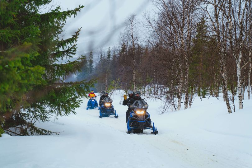 People driving snowmobiles through snowy nature.