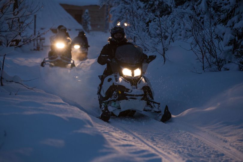 People driving snowmobiles through snowy nature