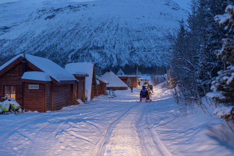 People driving snowmobiles through snowy nature