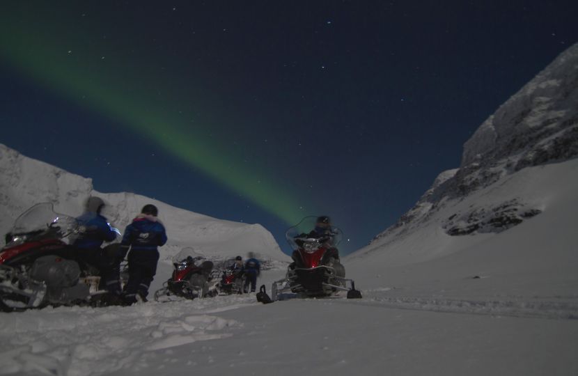 People standing next to snowmobiles and looking at Northern lights