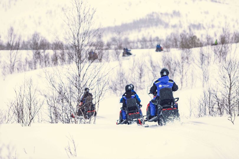 People driving snowmobiles through snowy nature.