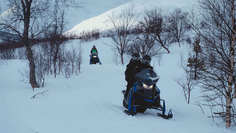 People driving snowmobiles through snowy nature.