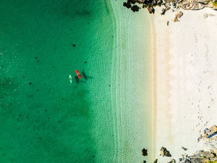 two people padleboarding by a white sandy beach in clear turquoise water