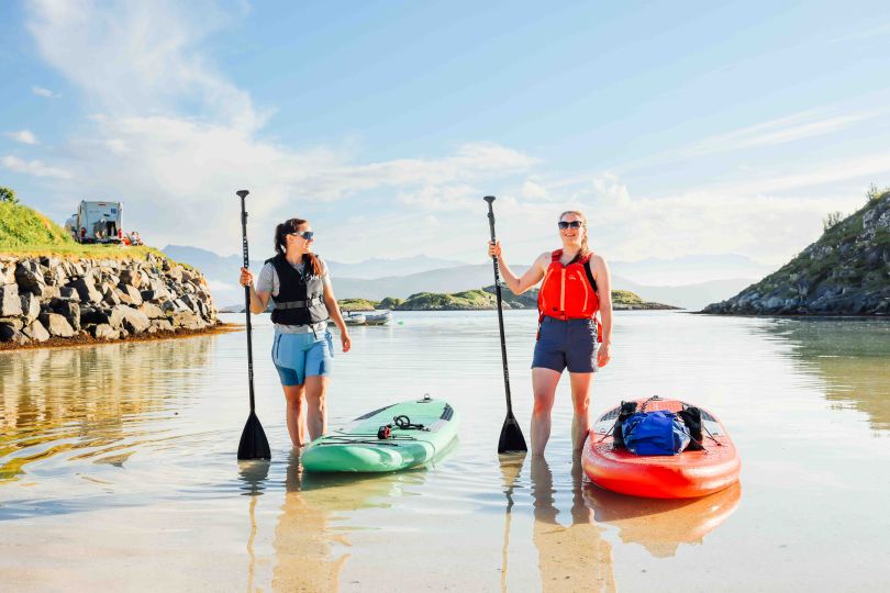 two people standing in the water smiling next to a couple of paddleboards by the beach