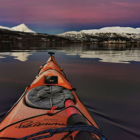 Winter kayaking in Tromso Norway with beautiful views of snow covered mountains and colourful winter sky